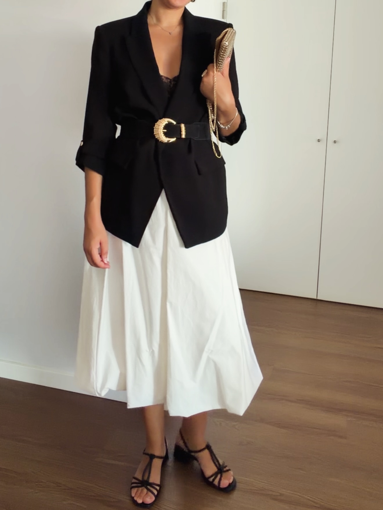 Look com blazer preto, cinto dourado e saia midi branca
